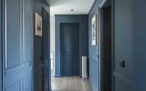 Peinture d'un couloir aux tons bleus profonds, avec des portes assorties et des cadres de portes ornés. Des tableaux discrets ornent les murs.