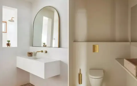 Idées pour décorer ses toilettes : un lavabo suspendu blanc, un miroir arche doré, une chasse d'eau dorée et une brosse WC assortie.