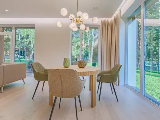 Éclairage salle à manger sans plafonnier : suspension moderne au-dessus d'une table ronde, entourée de chaises vertes. Lumière naturelle abondante des grandes fenêtres.