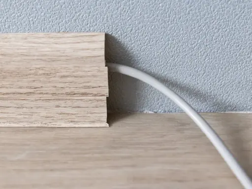Une plinthe en bois imite le bois et cache un fil électrique. Astuce pour comment cacher des fils électriques.
