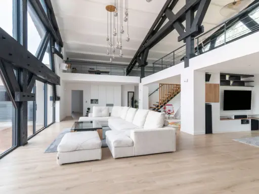 Salon moderne avec poutres apparentes, canapé blanc, escalier en bois. Ce style peut influencer le prix renovation appartement.