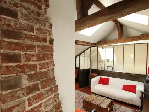 Aménagement combles idées : un salon cosy sous les toits avec murs en briques apparentes, poutres en bois et canapé blanc.