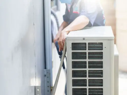 Un technicien s'occupe de recharger la clim de la maison. Il manipule des tuyaux près de l'unité extérieure.