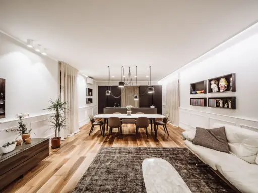 Un grand salon moderne avec un canapé blanc, une table à manger ovale et une cuisine intégrée. La taille du salon est optimisée pour le confort.