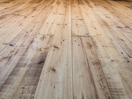 Planches de bois clair, usées et clouées, avec un parquet qui craque sous les pieds.