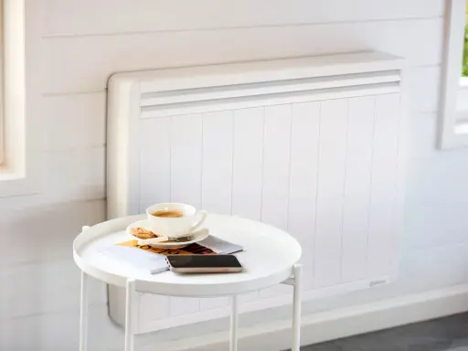 Un radiateur blanc moderne, idéal pour le chauffage maison neuve, avec une tasse de café et des magazines sur une table d'appoint.