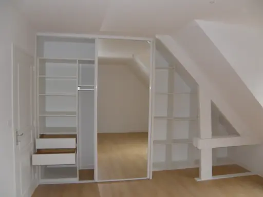 Aménagement astucieux pour faire un dressing sous pente. Étagères et tiroirs blancs s'intègrent parfaitement à l'espace mansardé.