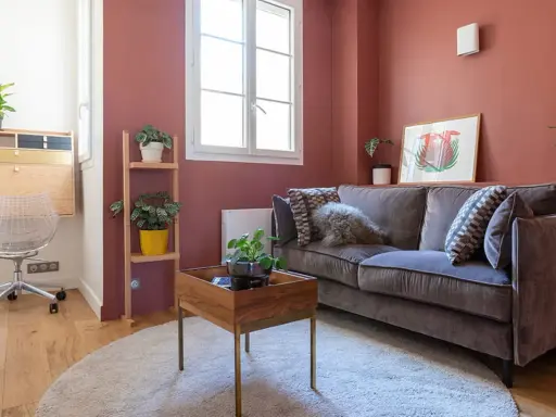 Chambre d'amis confortable avec un canapé convertible (clic clac) en velours gris, des plantes vertes et un bureau mural.