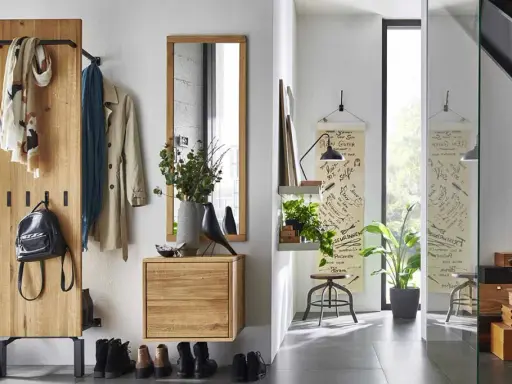 Une entrée dans un salon moderne avec un portant en bois, des manteaux, un sac à dos, des tableaux et une étagère avec des plantes.