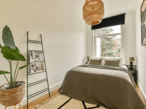 Chambre 9m2 avec salle de bain, lit douillet, plante verte et étagère murale. Luminaire en rotin au-dessus.