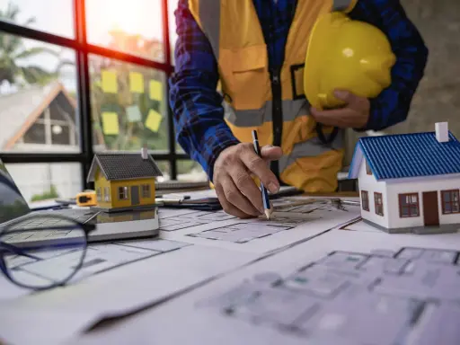 Un architecte examine des plans pour une maison ancienne, évaluant le DPE. Maquettes de maisons sur la table.