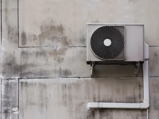 Unité extérieure d'une pompe à chaleur fixée sur un mur en béton. L'isolation est visible sur le tuyau blanc.