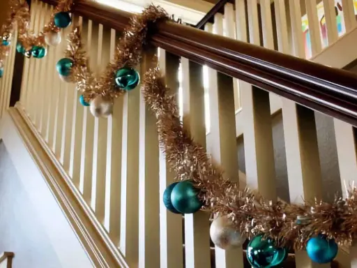 Guirlande dorée et boules de Noël bleues et blanches pour décorer une rampe d'escalier pour Noël.