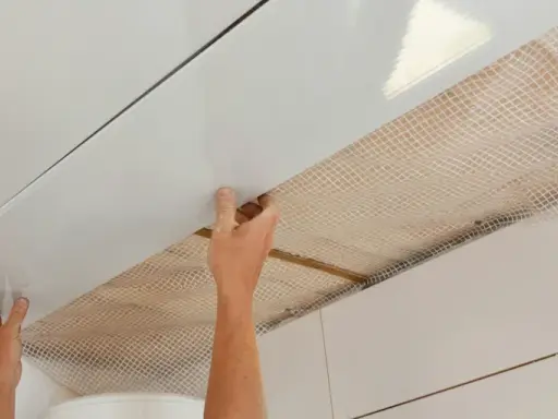 Mains installant des panneaux blancs pour refaire un plafond, avec un treillis visible en dessous.