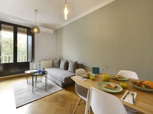 Un salon salle à manger de 20m2 prêt pour le petit-déjeuner, avec un canapé confortable, une table en bois garnie de croissants et de jus d'orange, et une grande fenêtre lumineuse.