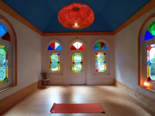 Un tapis de yoga orange attend dans une pièce lumineuse aux vitraux colorés, créant une atmosphère de maison bienveillante.