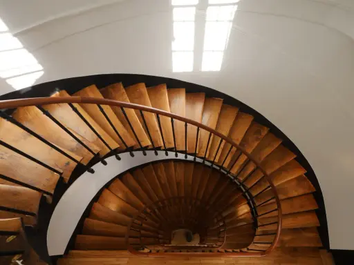 Vue plongeante d'un escalier en colimaçon en bois, parfait pour une rénovation cage escalier immeuble. La lumière naturelle illumine les marches.