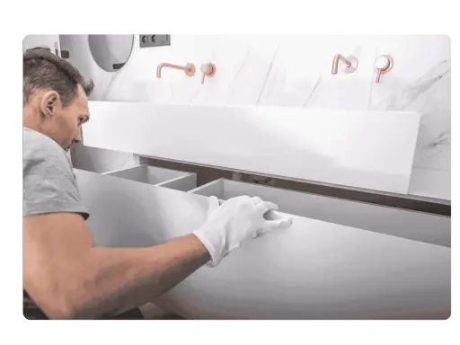 Un homme en gants blancs installe un meuble de salle de bain suspendu. Il s'assure de bien fixer meuble lourd sur placo pour une installation solide.