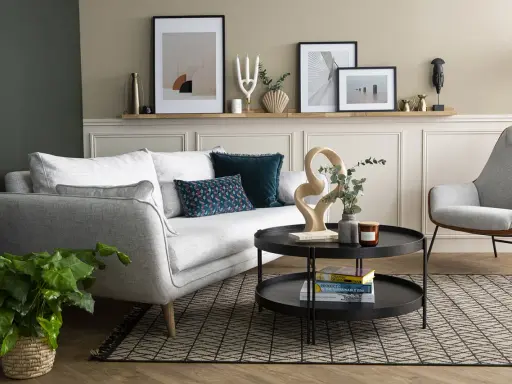 Salon moderne avec canapé gris clair, coussins décoratifs et une sculpture abstraite. La décoration murale au-dessus du canapé complète l'ensemble.