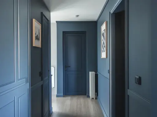 Peinture d'un couloir aux tons bleus profonds, avec des portes assorties et des cadres de portes ornés. Des tableaux discrets ornent les murs.