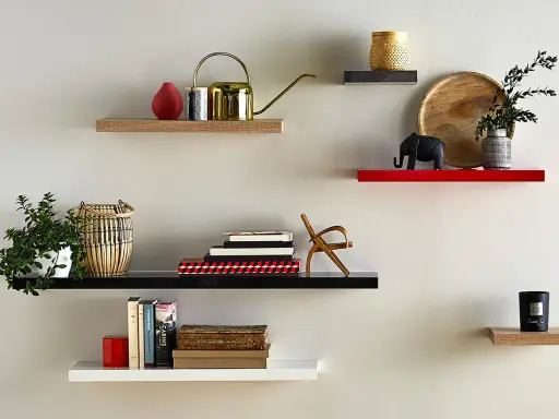 Étagères flottantes décorées : plante, arrosoir doré, livres, éléphant, bougie. La hauteur entre étagère varie pour un design dynamique.