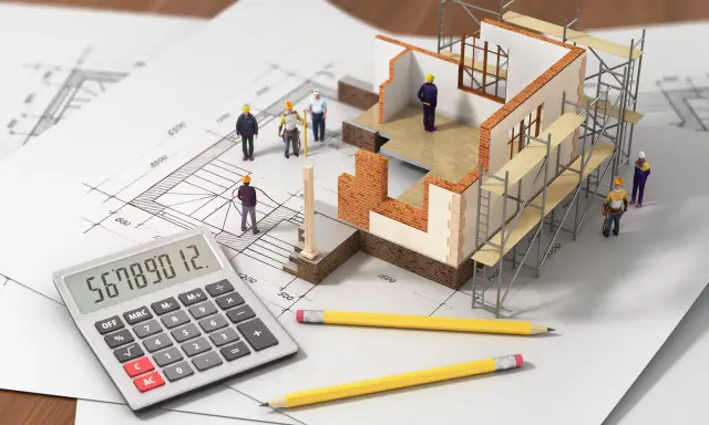 Maquette de maison en construction sur plans, avec des figurines d'ouvriers, une calculatrice et des crayons. L'inflation des matériaux de construction rend le calcul du budget complexe.