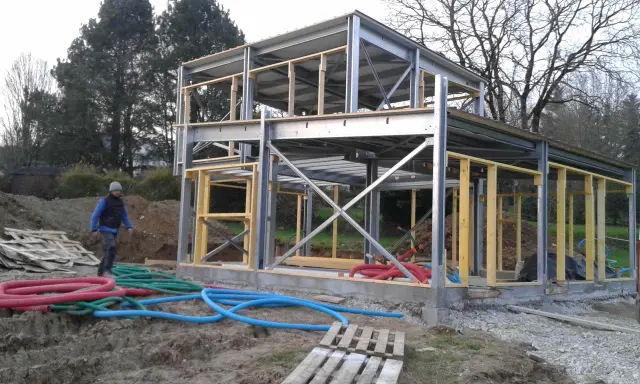 Chantier d'une maison ossature métallique, structure en acier et bois, avec des tuyaux colorés au sol.