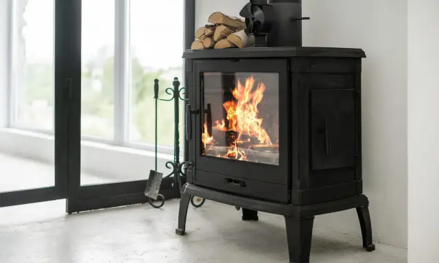 Poêle à bois en fonte avec flammes vives, pile de bois et accessoires. Idéal pour un couplage pompe à chaleur et poêle bois pour une chaleur optimale.