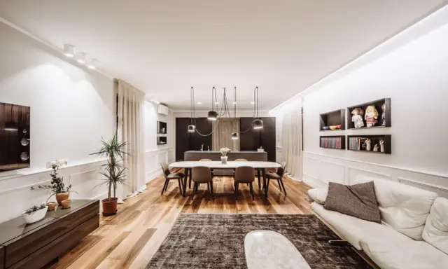 Un grand salon moderne avec un canapé blanc, une table à manger ovale et une cuisine intégrée. La taille du salon est optimisée pour le confort.