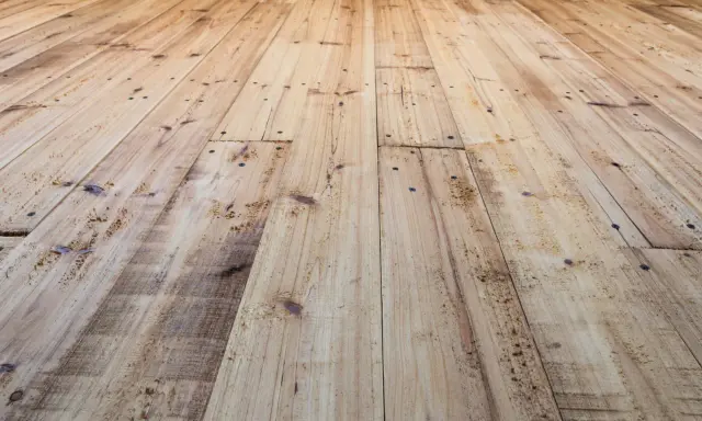 Planches de bois clair, usées et clouées, avec un parquet qui craque sous les pieds.