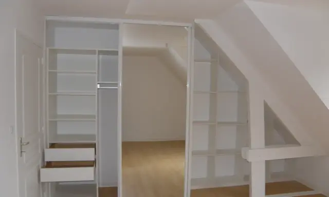Aménagement astucieux pour faire un dressing sous pente. Étagères et tiroirs blancs s'intègrent parfaitement à l'espace mansardé.