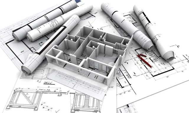 Maquette 3D d'une maison familiale sur des plans d'architecte, avec des rouleaux de plans et des stylos rouges.