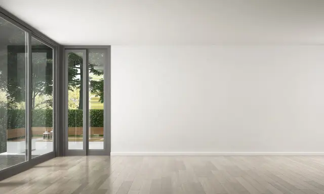 Un salon lumineux avec de grandes baies vitrées donnant sur un jardin verdoyant. Le parquet clair est parfait pour refaire le sol de la maison.