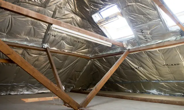 Isolation argentée sous les combles, avec poutres en bois et fenêtres de toit. Un système VMC sans comble est en cours d'installation.