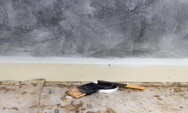Outils pour enduire un mur abîmé : spatules et pot de mastic sur une bâche de protection au sol.