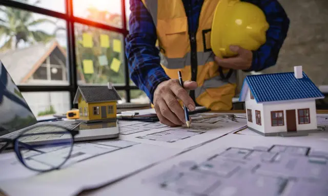 Un architecte examine des plans pour une maison ancienne, évaluant le DPE. Maquettes de maisons sur la table.
