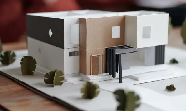 Maquette d'une maison individuelle moderne aux lignes épurées, avec des éléments en carton et des arbres stylisés.