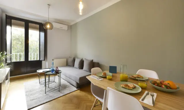 Un salon salle à manger de 20m2 prêt pour le petit-déjeuner, avec un canapé confortable, une table en bois garnie de croissants et de jus d'orange, et une grande fenêtre lumineuse.