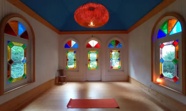 Un tapis de yoga orange attend dans une pièce lumineuse aux vitraux colorés, créant une atmosphère de maison bienveillante.