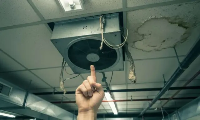 Une main pointe un VMC bruyant au plafond, à côté d'une tache d'humidité.