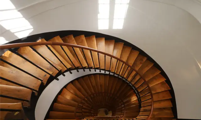Vue plongeante d'un escalier en colimaçon en bois, parfait pour une rénovation cage escalier immeuble. La lumière naturelle illumine les marches.