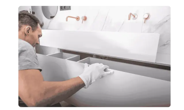 Un homme en gants blancs installe un meuble de salle de bain suspendu. Il s'assure de bien fixer meuble lourd sur placo pour une installation solide.