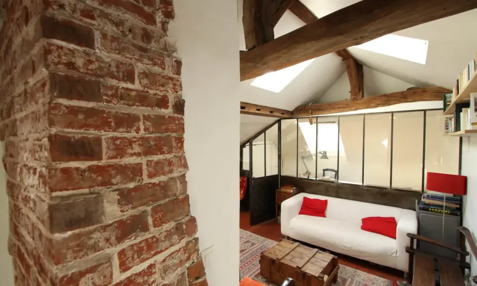 Aménagement combles idées : un salon cosy sous les toits avec murs en briques apparentes, poutres en bois et canapé blanc.