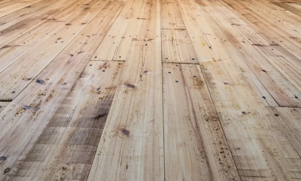 Planches de bois clair, usées et clouées, avec un parquet qui craque sous les pieds.