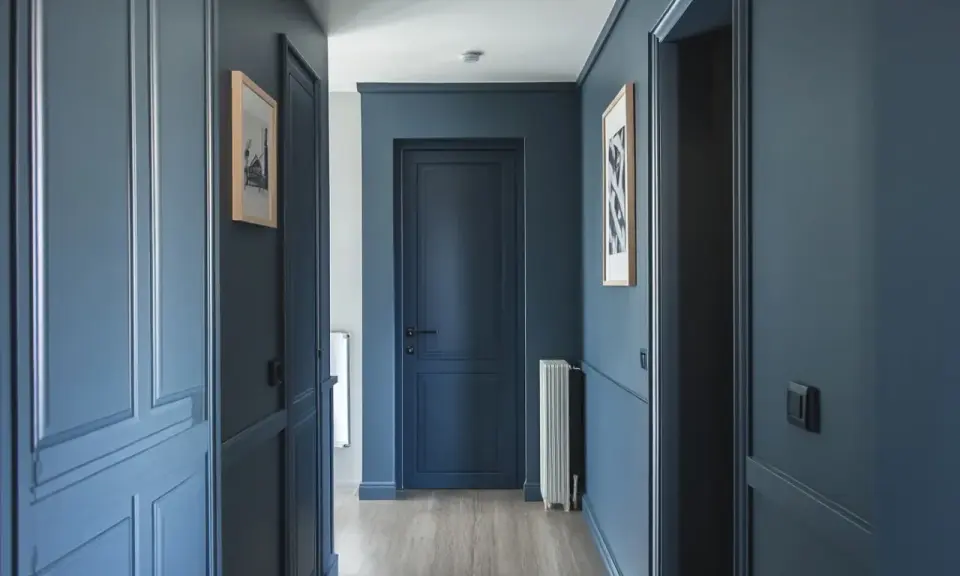 Peinture d'un couloir aux tons bleus profonds, avec des portes assorties et des cadres de portes ornés. Des tableaux discrets ornent les murs.