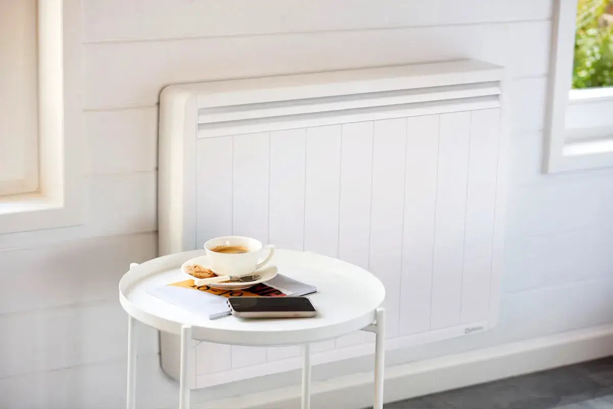 Un radiateur blanc moderne, idéal pour le chauffage maison neuve, avec une tasse de café et des magazines sur une table d'appoint.
