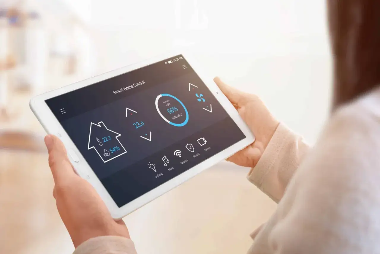 Une personne utilise une tablette pour contrôler son cee thermostat connecté, ajustant la température et l'éclairage de sa maison.
