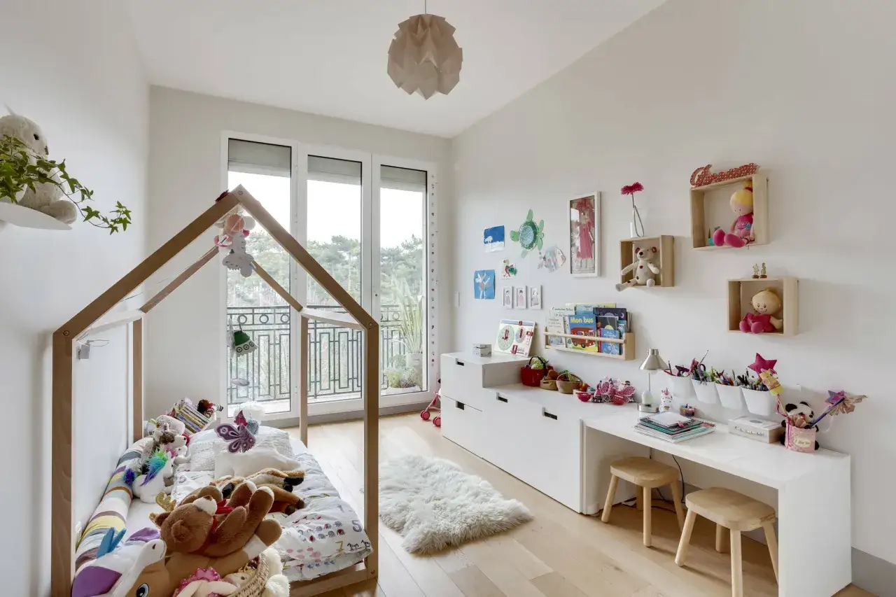 Chambre fille petit espace : lit cabane, peluches, bureau et étagères décorées.