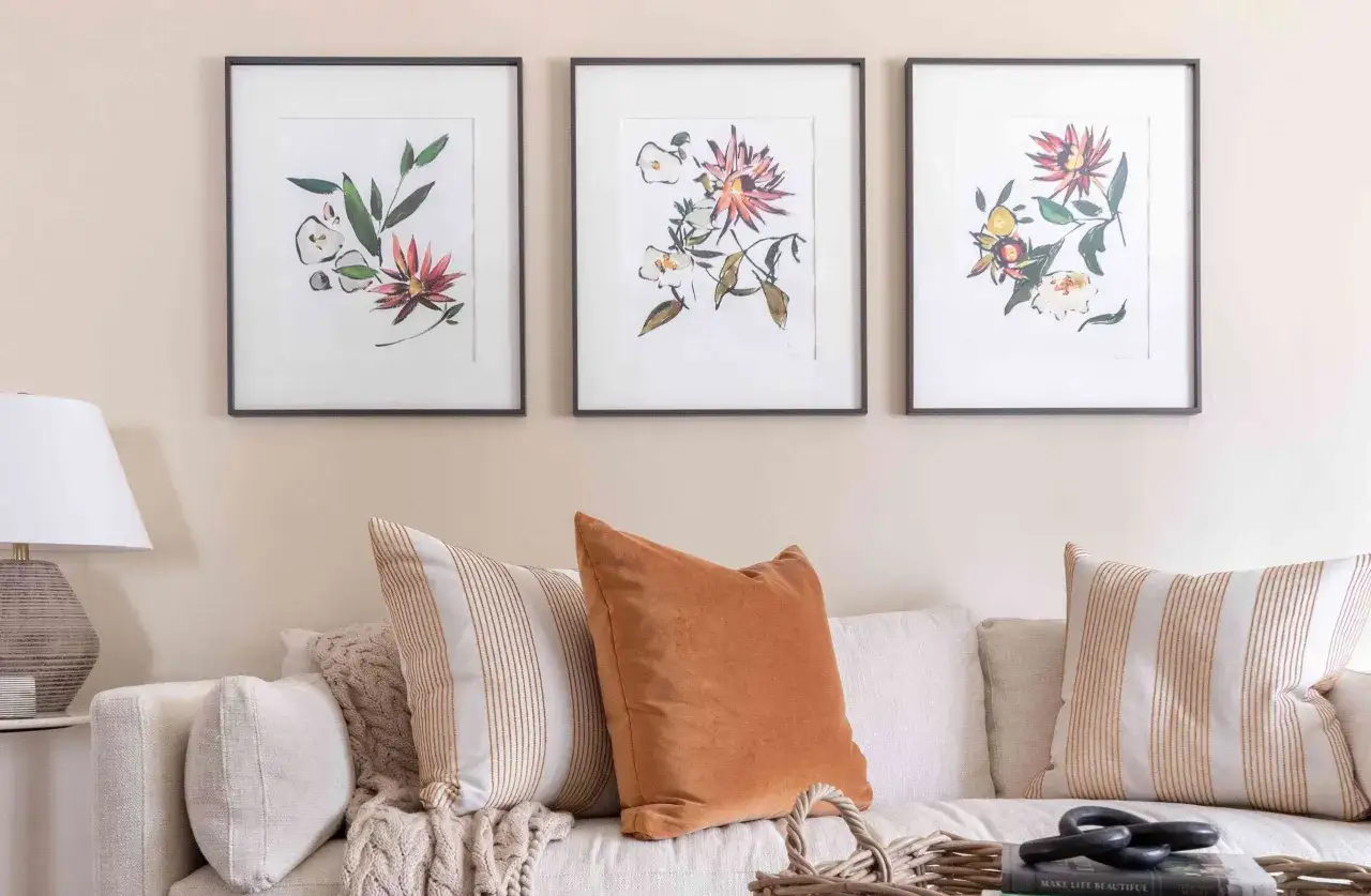Disposition 3 cadres avec des aquarelles de fleurs et de feuilles vertes, pos&eacute;s au-dessus d'un canap&eacute; confortable avec des coussins textur&eacute;s.