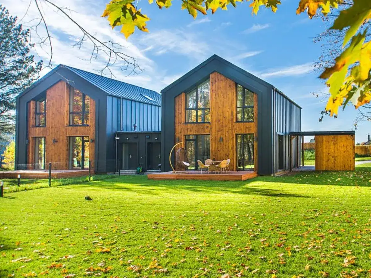 Deux maisons modernes en bois et métal, une maison éco responsable avec de grandes fenêtres, sur une pelouse verte sous un ciel bleu.